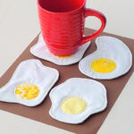 Red mug with four sunny side up egg coasters.